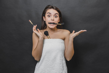 Obraz premium Portrait of young beautiful girl wears white towel and holds make up brush in teeth.