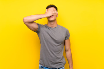 Handsome man over isolated yellow wall covering eyes by hands. Do not want to see something