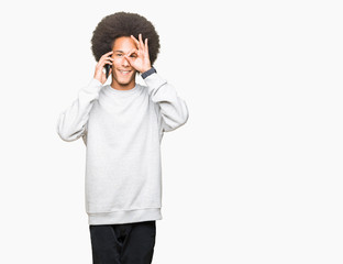 Young african american man with afro hair talking on smartphone with happy face smiling doing ok sign with hand on eye looking through fingers