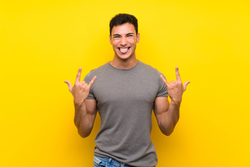 Handsome man over isolated yellow wall making rock gesture