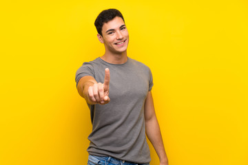 Handsome man over isolated yellow wall showing and lifting a finger