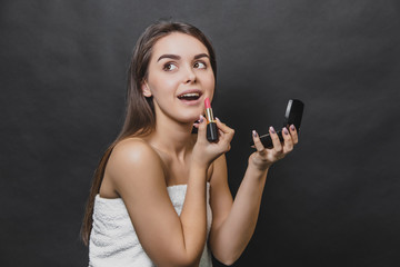 Obraz premium Beautiful girl paints her lips with red lipstick. Skin care concept. Looking up and rightwards.