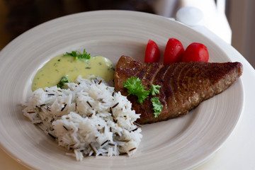 Fried slice of tuna with rice on garnish with sauce on white plate