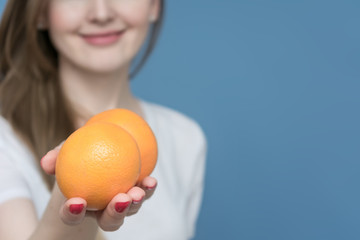 Young beautiful girl offer you an oranges at the camera, blue background, copy space