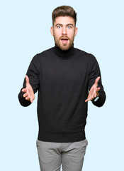 Fototapeta premium Young handsome blond man wearing winter sweater afraid and shocked with surprise expression, fear and excited face.