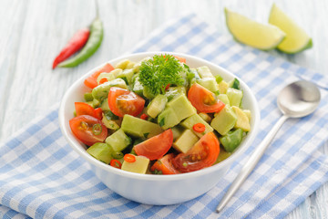 Salsa from avocado, cherry tomatoes and lime. Traditional salad from fresh vegetables with avocado. A serving is serialized in a deep white bowl on a blue napkin.