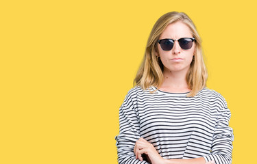 Beautiful young woman wearing sunglasses over isolated background skeptic and nervous, disapproving expression on face with crossed arms. Negative person.