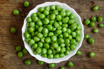 Fresh green peas in a white plate on wooden background, top view. Rustic table background