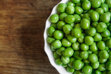 Fresh green peas in a white plate on wooden background, top view. Rustic table background