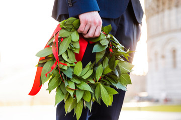 Giovane laureato con corona d'alloro verde e nastro rosso tenuto in mano. Cerimonia di laurea.