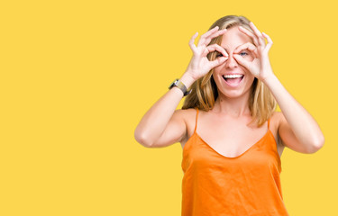 Beautiful young woman wearing orange shirt over isolated background doing ok gesture like binoculars sticking tongue out, eyes looking through fingers. Crazy expression.