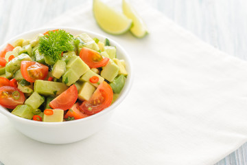 Salsa from avocado, cherry tomatoes and lime. Traditional salad from fresh vegetables with avocado. A serving is serialized in a deep white bowl on a white napkin. Close up and horizontal orientation.