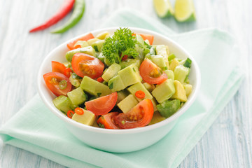 Salsa from avocado, cherry tomatoes and lime. Traditional salad from fresh vegetables with avocado. A serving is serialized in a deep white bowl on a blue napkin. Space for text.