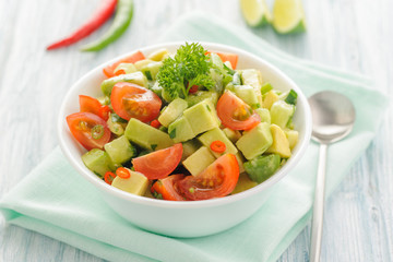 Salsa from avocado, cherry tomatoes and lime. Traditional salad from fresh vegetables with avocado. A serving is serialized in a deep white bowl on a blue napkin. Close up and horizontal orientation.