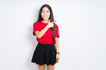Fototapeta premium Beautiful brunette woman wearing red t-shirt and skirt over isolated background cheerful with a smile of face pointing with hand and finger up to the side with happy and natural expression on face
