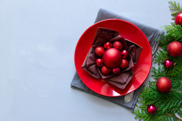 Christmas table setting with red plate, brown napkin in lotos shape and balls on gray wooden background. Holiday decorations concept. Flat lay. Top view. Copy space