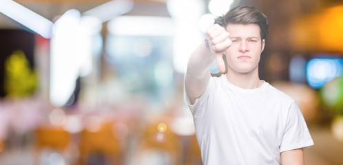 Young handsome man wearing casual white t-shirt over isolated background looking unhappy and angry showing rejection and negative with thumbs down gesture. Bad expression.