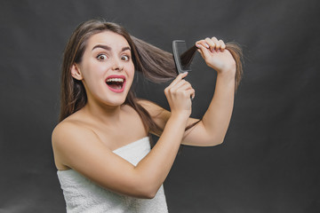 Obraz premium Young pretty girl brushing her hair and looking for hair falling on the comb and hands on a black background. Hair care, pain when combing. A frightened girl lifting her hair, opening her mouth.