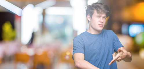 Young handsome man wearing blue t-shirt over isolated background In hurry pointing to watch time,...