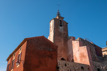 Fototapeta premium Roussillon, France: church tower and buildings facade with the ochre color with clean blue sky as background