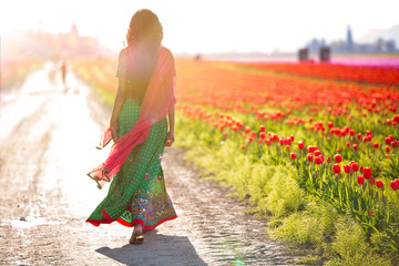 Beautiful Indian woman walking away in a field of tulips - Powered by Adobe