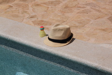 Sonnenhut und Federball liegen am Swimmingpool im Urlaub