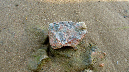The photo shows a medium-sized stone, it lies on the sand, under it you can see other stones buried...