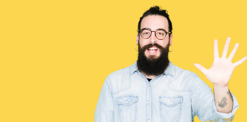 Naklejka premium Young hipster man with long hair and beard wearing glasses showing and pointing up with fingers number five while smiling confident and happy.