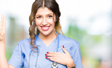 Young adult doctor woman wearing medical uniform Swearing with hand on chest and fingers, making a...