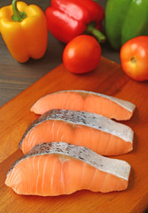 Vertical image of raw salmon slices on wooden cutting board with fresh vegetables