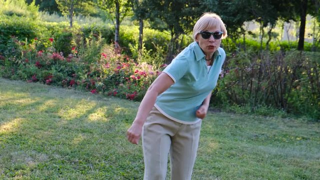 Mature cheerful woman dancing in the park, slow motion