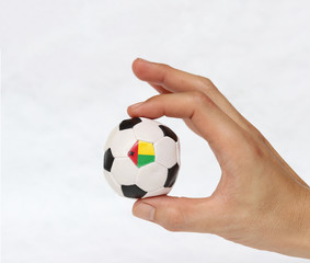 Fototapeta premium Mini ball of football in hand and one black point of football is Guinea bissau flag, hold it with two finger on white background.