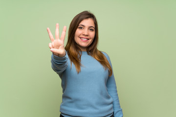 Young girl over green wall happy and counting three with fingers