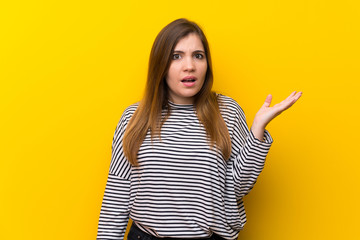 Young girl over yellow wall making doubts gesture