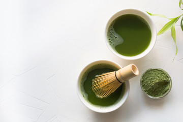 Two bowl green matcha tea and bamboo whisk on white concrete table. Top view.