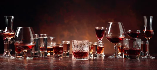 Plexiglas foto achterwand Set van sterke alcoholische dranken in glazen op een bruine achtergrond. © Igor Normann