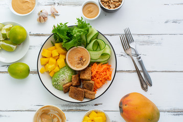 Healthy summer fresh salad with mango, avocado, lime and tofu with sweet peanut butter dressing on white wooden table