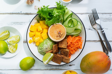 Healthy summer fresh salad with mango, avocado, lime and tofu with sweet peanut butter dressing on white wooden table