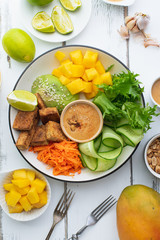 Healthy summer fresh salad with mango, avocado, lime and tofu with sweet peanut butter dressing on white wooden table