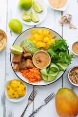 Healthy summer fresh salad with mango, avocado, lime and tofu with sweet peanut butter dressing on white wooden table