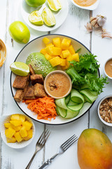 Healthy summer fresh salad with mango, avocado, lime and tofu with sweet peanut butter dressing on white wooden table