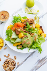 Healthy summer fresh salad with mango, avocado, lime and tofu with sweet peanut butter dressing on white wooden table