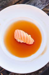 A nigiri sushi with salmon in soy sauce on white plate.