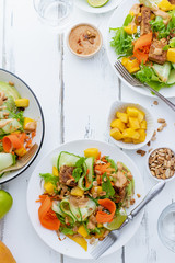 Healthy summer fresh salad with mango, avocado, lime and tofu with sweet peanut butter dressing on white wooden table