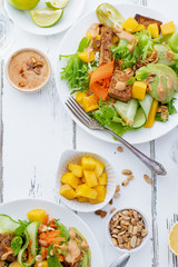 Healthy summer fresh salad with mango, avocado, lime and tofu with sweet peanut butter dressing on white wooden table