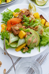 Healthy summer fresh salad with mango, avocado, lime and tofu with sweet peanut butter dressing on white wooden table