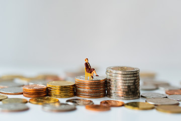 Miniature people, businesswoman sitting on stack coins using as business and financial concept