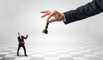 Small businessman fighting against big chessman on a big hand with chess board concept
