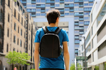 Rear view of a young man with backpack just arrived in a big city and looking to modern buildings...