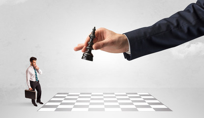 Little businessman thinking about chess strategy with a big hand concept
